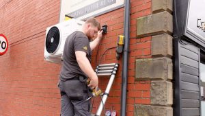 Image of an RJ Martindale expert engineer fitting a condenser unit outside a property, where they are installing air conditioning