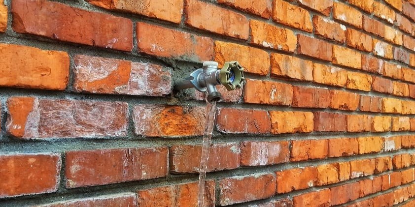 Outdoor tap attached onto a red brick wall with fresh water running from it
