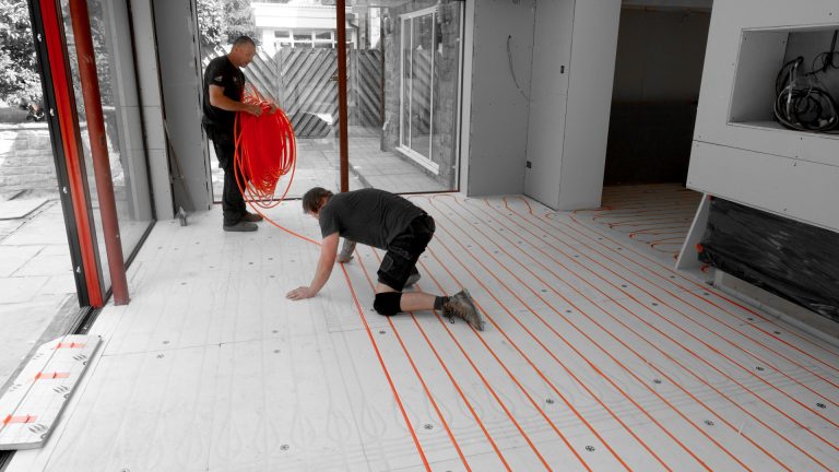 RJ Martindale engineers laying underfloor heating flexible plastic pipes in a loop across the floor on top of insulation boards
